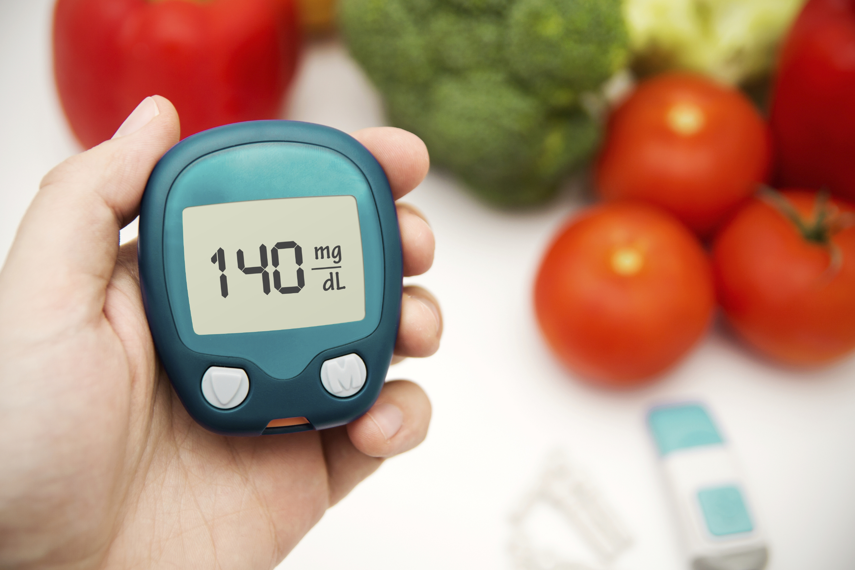 Hand holding meter. Diabetes doing glucose level test. Vegetables in background